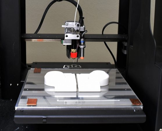 Photo of a 3D printer printing an object on a glass bed.